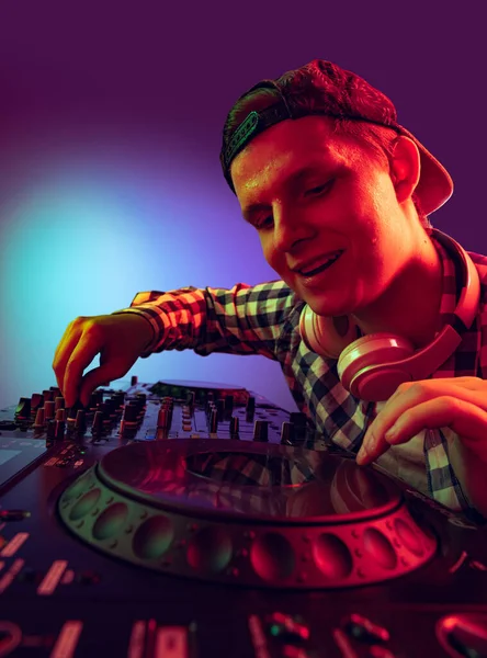 Porträtt av ung pojke i casual tyg, parti dj gör musik med professionell ljud mixer isolerad över lila bakgrund i neon ljus — Stockfoto