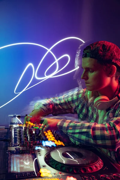 Günlük giysiler içinde genç bir çocuğun portresi, parti DJ 'i profesyonel ses mikseriyle müzik yapıyor mor arka planda, neon ışıkta izole edilmiş.