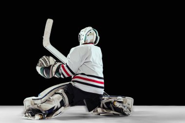 Genç bir çocuğun dinamik portresi, hareket halindeki hokey oyuncusu, siyah stüdyo arka planında izole edilmiş eğitim. Profesyonel kaleci.
