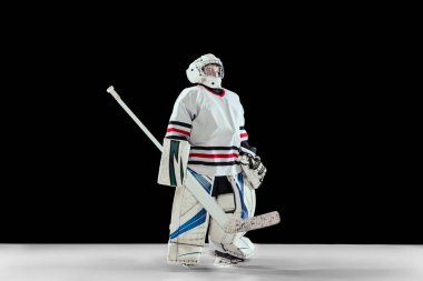 Genç bir çocuğun tam boy portresi, özel koruyucu üniformalı hokey oyuncusu, siyah stüdyo arka planında izole edilmiş bir kaleci.