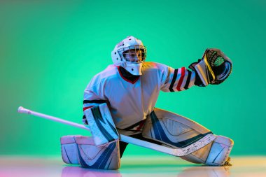 Çocuğun dinamik portresi, hokey oyuncusu, top yakalayan kaleci özel eldiven ile yeşil arka planda izole edilmiş neon ışığı.