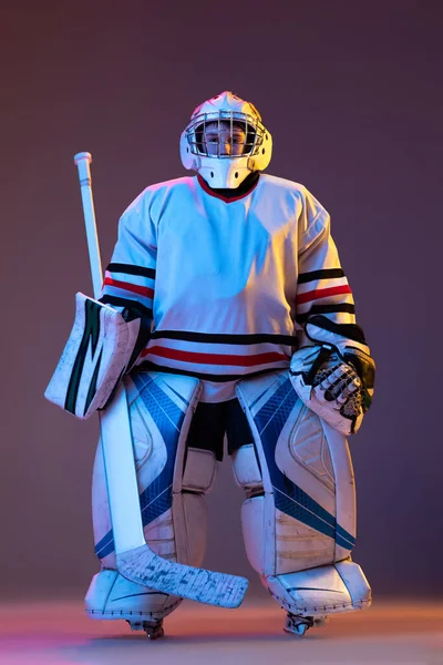 Portrait of boy, child posing in protective hockey uniform of goalkeeper isolated over purple background in neon light — 스톡 사진