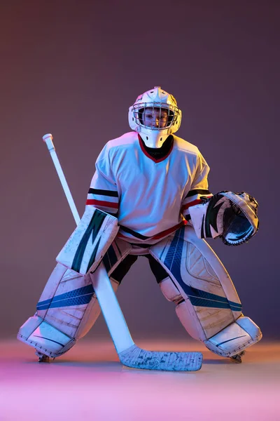 Portrait of concentrated boy, child, goalkeeper, training hockey game isolated over purple background in neon light — 스톡 사진