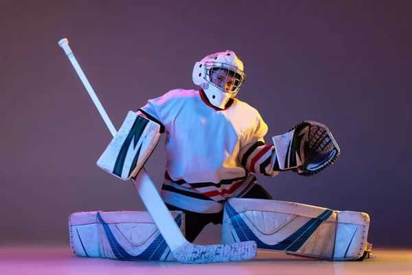 Portrait of teen boy, hockey player, goalkeeper catching puck with special glove isolated on purple background in neon light — 스톡 사진