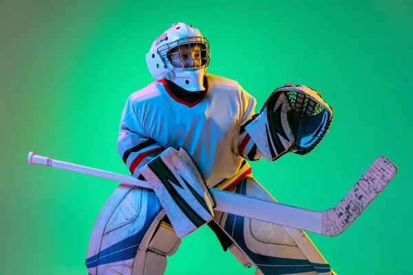 Dynamiskt porträtt av tonåring pojke, hockeyspelare, målvakt fånga puck med särskild handske isolerad på grön bakgrund i neon ljus — Stockfoto