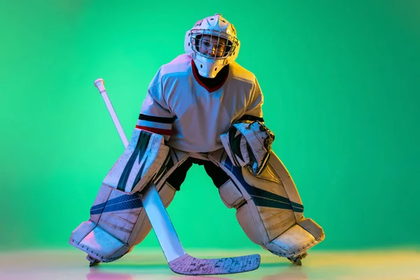 Full-length portrait of boy, hockey player, goalkeeper training, playing isolated over green background in neon light — 스톡 사진