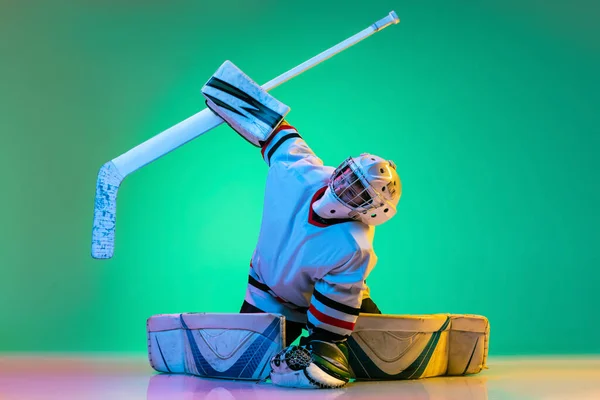 Full-length portrait of young boy, hockey player training, goalkeeper in action isolated on green background in neon ligh. Sportive childhood — 스톡 사진
