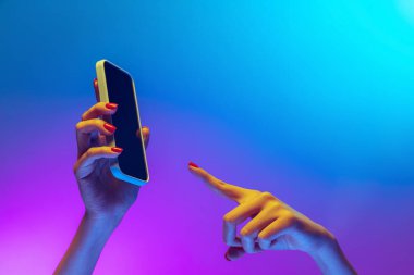 Yakın çekimde kadın elleri alet tutuyor, akıllı telefon neon rengi mavi ve mor arka planda izole edilmiş. Taşınabilir yaşam tarzı kavramı, dijital teknoloji, sosyal toplanma.