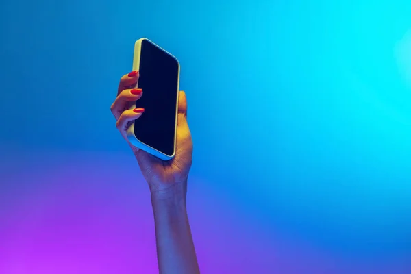 Close-up mãos femininas segurando gadget, smartphone isolado no gradiente azul e roxo de fundo em néon. Conceito de estilo de vida móvel, tecnologia digital, reunião social. — Fotografia de Stock