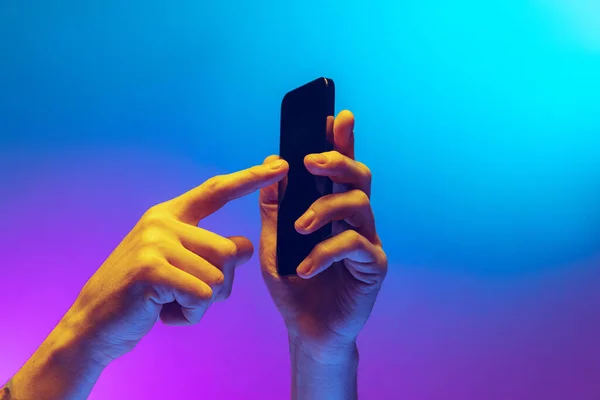 Mãos masculinas close-up segurando gadget, smartphone isolado no gradiente azul e fundo roxo em néon. Conceito de estilo de vida móvel, tecnologia digital, reunião social. — Fotografia de Stock