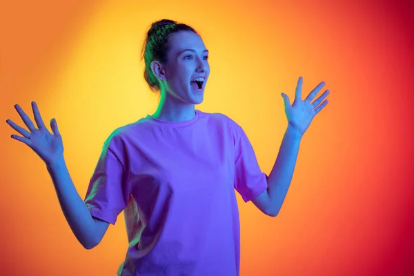 Half-length portrait of young surprised girl, student with long hair posing isolated on orange background in neon light, filter. Concept of emotions, youth, beauty — Stock fotografie