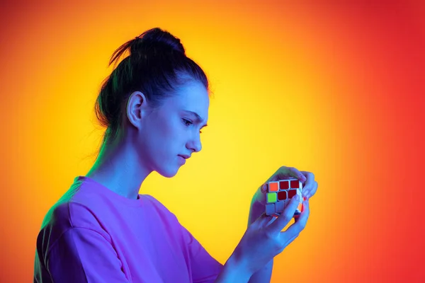 Half-length portrait of young charming girl, student with long hair posing isolated on orange background in neon light, filter. Concept of emotions, youth, beauty. Side view — 스톡 사진