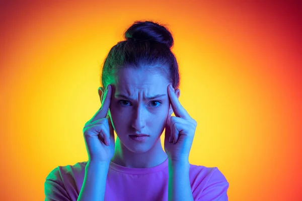 Half-length portrait of young charming girl, student with long hair posing isolated on orange background in neon light, filter. Concept of emotions, youth, beauty — Stock Fotó