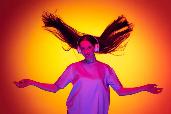 Emotional caucasian girl wearingt-shirt dancing, listening to music isolated on yellow-red background in neon. Concept of beauty, art, fashion, youth and emotions — Stockfoto