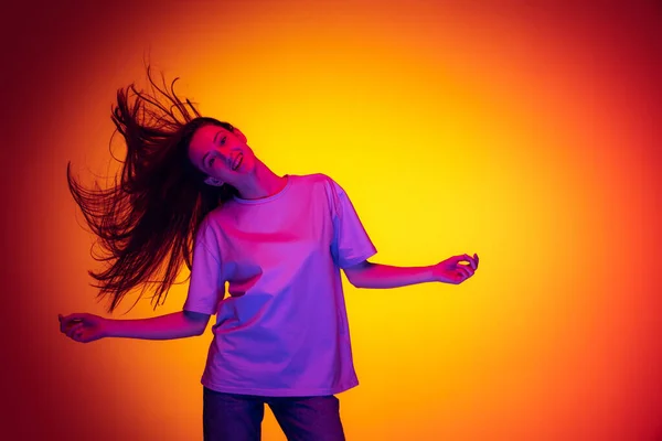 Emotionele blanke meisje dragen-shirt dansen, plezier geïsoleerd op geel-rode achtergrond in neon. Concept van schoonheid, kunst, mode, jeugd en emoties — Stockfoto