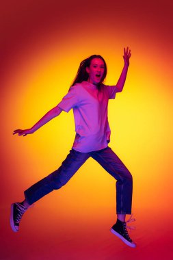 Full-length portrait of young cheerful girl, student with long hair jumping isolated on orange background in neon light, filter. Concept of emotions, youth, beauty