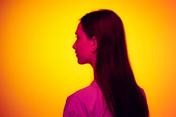 Vista traseira. Retrato de menina bonita jovem com cabelo longo brilhante isolado no fundo de cor amarela no filtro de néon. Conceito de emoções, beleza, moda, juventude. — Fotografia de Stock