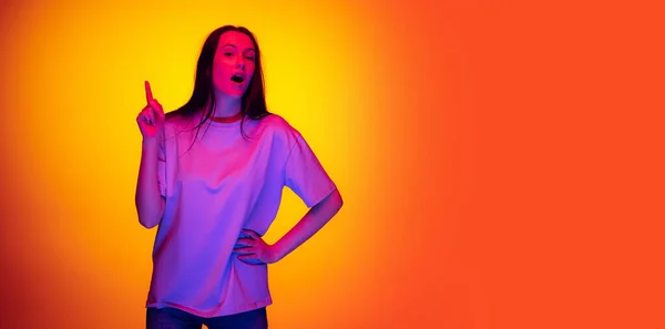 Flyer met portret van jong charmant meisje, student met lang haar poseren geïsoleerd op oranje achtergrond in neon licht, filter. Concept van emoties, jeugd, schoonheid — Stockfoto