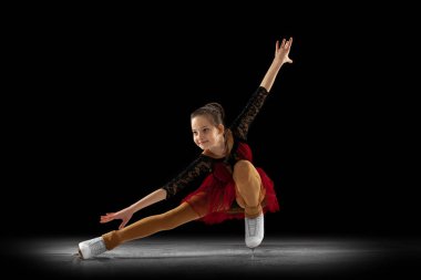 Güzel kız, sahnedeki güzel paten giyen küçük bayan artistik patinajcı sahne ışıkları altında siyah arka planda izole edilmiş. Hareket, spor, güzellik kavramı.