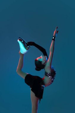 Genç kızın dinamik portresi, siyah sahne elbisesi giymiş kadın buz patenci mavi arka planda izole edilmiş neon ışıkta. Spor anlayışı, güzellik, aktif yaşam tarzı.