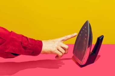 Colorful bright image of male finger touching retro iron isolated over pink yellow background