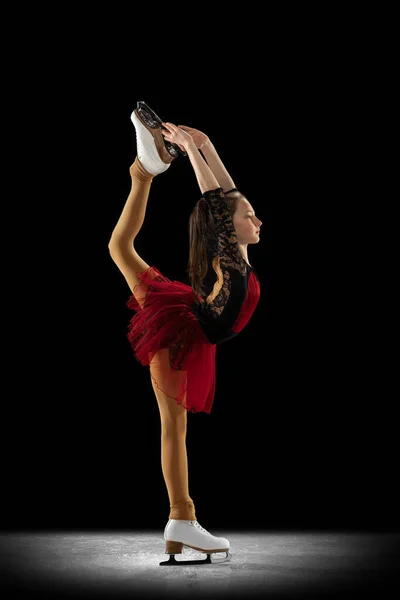 Studio shot of little female figure skater in beautiful stage attire skating isolated on black background in spotlight. Concept of movement, sport, beauty. — Photo