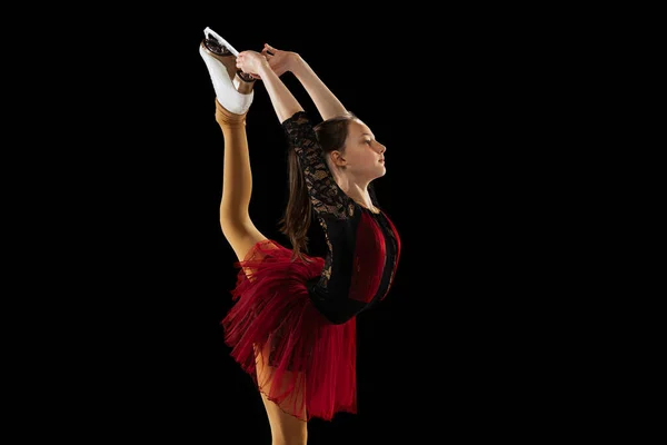 Studio shot of little female figure skater in beautiful stage attire skating isolated on black background in spotlight. Concept of movement, sport, beauty. — Stock Photo, Image