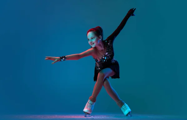 Retrato dinámico de niña, patinadora femenina en vestido de escenario negro patinaje aislado sobre fondo azul en luz de neón. Concepto de deporte, belleza, estilo de vida activo. —  Fotos de Stock