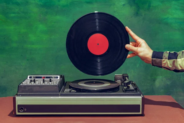 Colorful image of male hand holding retro vinyl record in front of vintage player isolated over dark green background — Fotografia de Stock