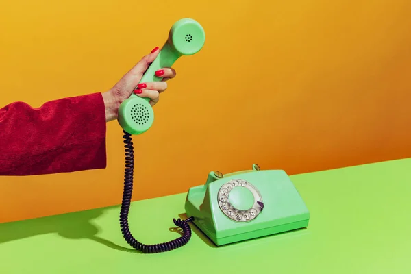 Colorful bright image of female hand holding old-fashioned green colored phone, picking up handset isolated over orange background — стоковое фото