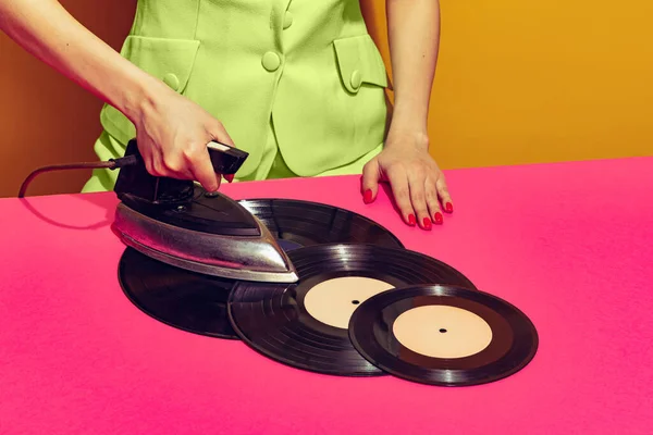 Colorful bright image of woman using retro iron and ironing vintage vinyl records isolated over pink background. — Foto Stock