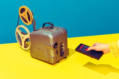 Pop art photography. Colorful image of retro film player on yellow bright tablecloth isolated over blue background. Movie time
