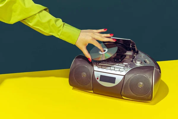 Colorful image of vintage radio player on bright yellow tablecloth isolated over dark green background. Putting music disk — 스톡 사진
