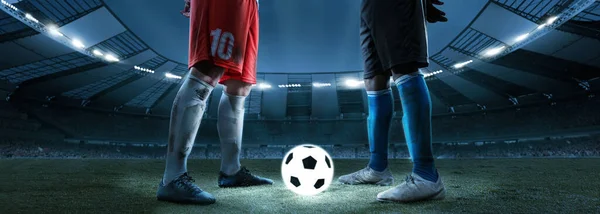 Night football match. Cropped image of two soccer, football players standing near luminous ball at stadium in evening. Concept of sport, competition, goals — ストック写真