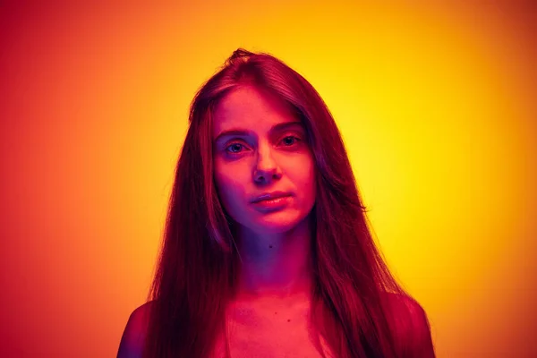 Portrait of young girl calmly looking at camera, posing isolated over gradient red yellow background in neon light — Stok fotoğraf