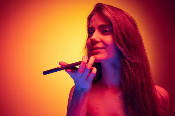 Retrato de niña grabando mensaje de voz en el teléfono aislado sobre el gradiente rojo amarillo fondo en luz de neón — Foto de Stock