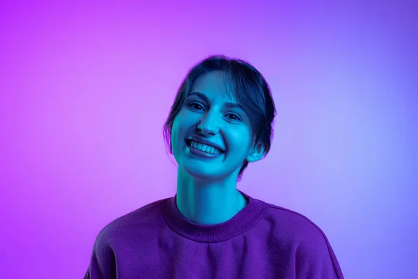 Portrait of young charming girl, student posing isolated over purple studio background in neon light. Concept of emotions, facial expression, art, beauty — Stock Fotó