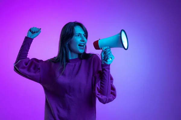 One young excited girl, student shouting at megaphone isolated over purple studio background in neon light. Concept of emotions, news, ad — Stock fotografie