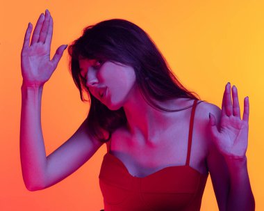Young funny girl, student leaned against transparent glass isolated on orange color background. Close-up.
