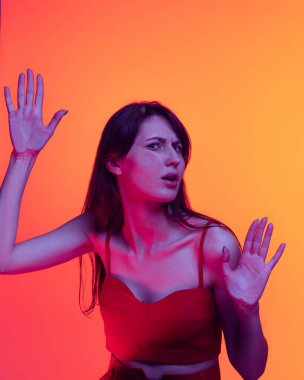 Genç komik kız, portakal rengi arka planda şeffaf cama yaslanmış öğrenci. Yakın plan..