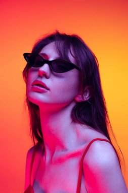Güneş gözlüklü şık bir model. Genç, parlak saçlı, kırmızı-sarı arka planda izole edilmiş güzel bir kız. Duygular, sanat, güzellik kavramı
