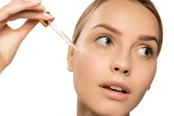 Close up beautiful young woman applying serum, oil on face on white background. Concept of cosmetics, makeup, natural beauty — Stok fotoğraf