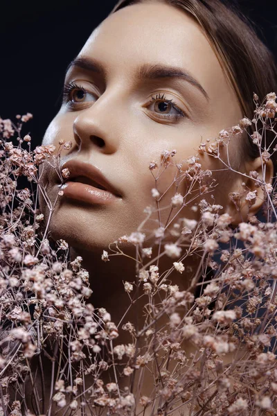 Retrato de close-up de bela jovem com pele limpa e bem conservada isolada em fundo escuro com flores. Conceito de beleza, arte, anúncio, cosméticos — Fotografia de Stock