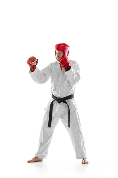 Portrait of young sportive man wearing white dobok, helmet and gloves practicing isolated over white background. Concept of sport, workout, health. — Stock fotografie