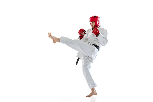 Portrait of young sportive man, taekwondo fighter wearing white dobok, helmet and gloves practicing isolated over white background. Concept of sport, workout, health. — Stockfoto