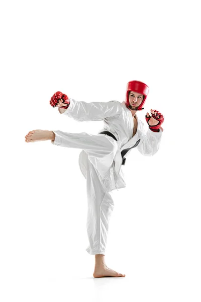 Portrait of young sportive man wearing white dobok, helmet and gloves practicing isolated over white background. Concept of sport, workout, health. — Foto de Stock
