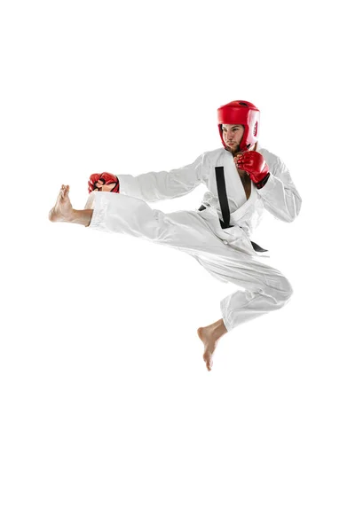 Portrait of young sportive man wearing white dobok, helmet and gloves practicing isolated over white background. Concept of sport, workout, health. — Foto de Stock