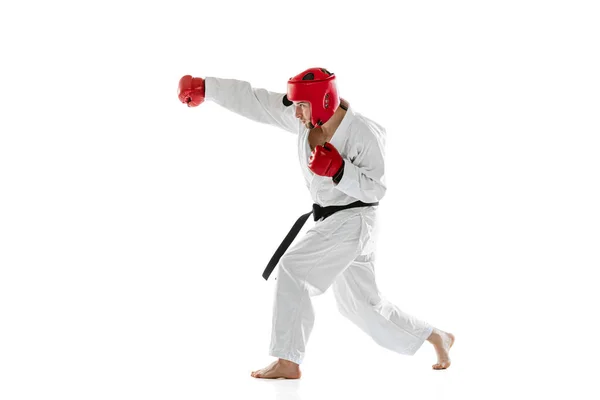 Portrait of young sportive man wearing white dobok, helmet and gloves practicing isolated over white background. Concept of sport, workout, health. — Stock Fotó
