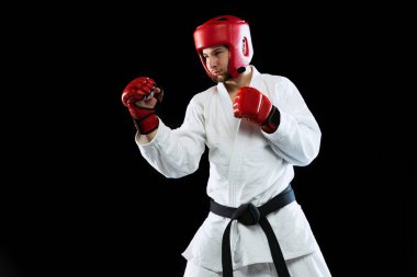 Male taekwondo fighter in white dobok, helmet and gloves training isolated over dark background. Concept of sport, workout, competition, ad