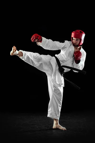 Caça taekwondo macho em dobok branco, capacete e luvas de treinamento isolado sobre fundo escuro. Conceito de esporte, treino, competição, anúncio — Fotografia de Stock